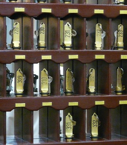 Reihe von Hotelzimmer-Schlüsseln mit goldenen Anhängern in einem Holzregal.