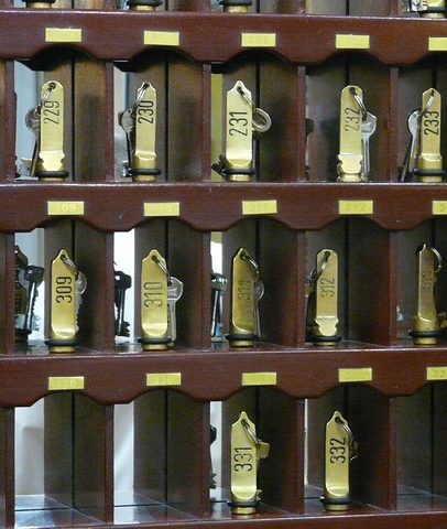 Reihe von Hotelzimmer-Schlüsseln mit goldenen Anhängern in einem Holzregal.