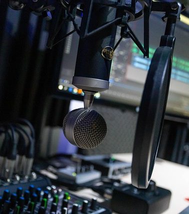Mikrofon vor einem Computerbildschirm mit Audioequipment im Hintergrund.