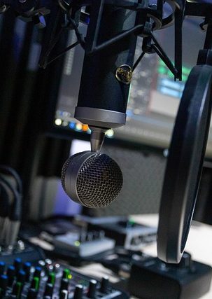 Mikrofon vor einem Computerbildschirm mit Audioequipment im Hintergrund.